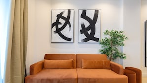 A modern living room with a sofa, a plant, and two abstract paintings on the wall. - M Agu230 Tu Hogar en la Ciudad Piso de 3 Habita (Madrid)