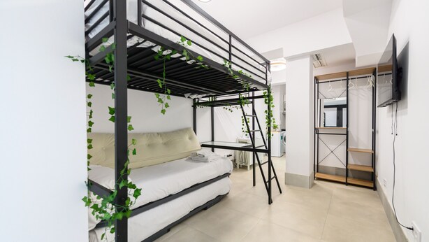 A bunk bed with a ladder, a sofa, and a television mounted on the wall. - M Rjs3 Acogedor Estudio en Barrio Salamanca (Madrid)
