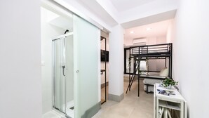 A modern hotel room with a glass shower door, a bunk bed, a small table with a plant, and a white cabinet. - M Rjs3 Acogedor Estudio en Barrio Salamanca (Madrid)