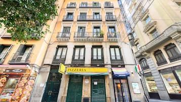 A building with a pizzeria on the ground floor, featuring a green awning and a sign with the word "PIZZERIA".
