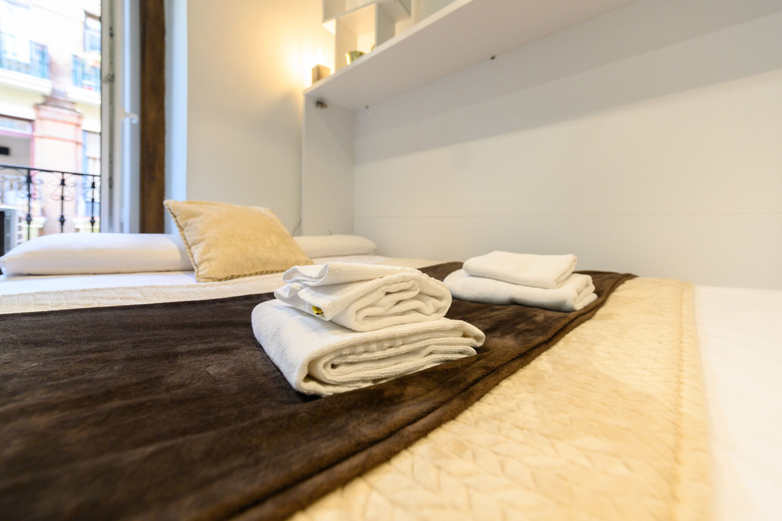 A neatly made bed with a brown cover, white pillows, and folded towels.