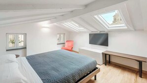 Un dormitorio moderno con cama, escritorio, silla, televisor y tragaluces.