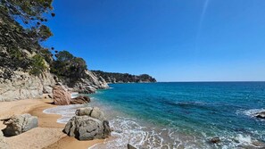 A coastal beach with clear blue waters, rocky cliffs, and a small settlement in the distance. - Kerstin Bruns - Apartment with an ocean view and air conditioning (Tossa de Mar)