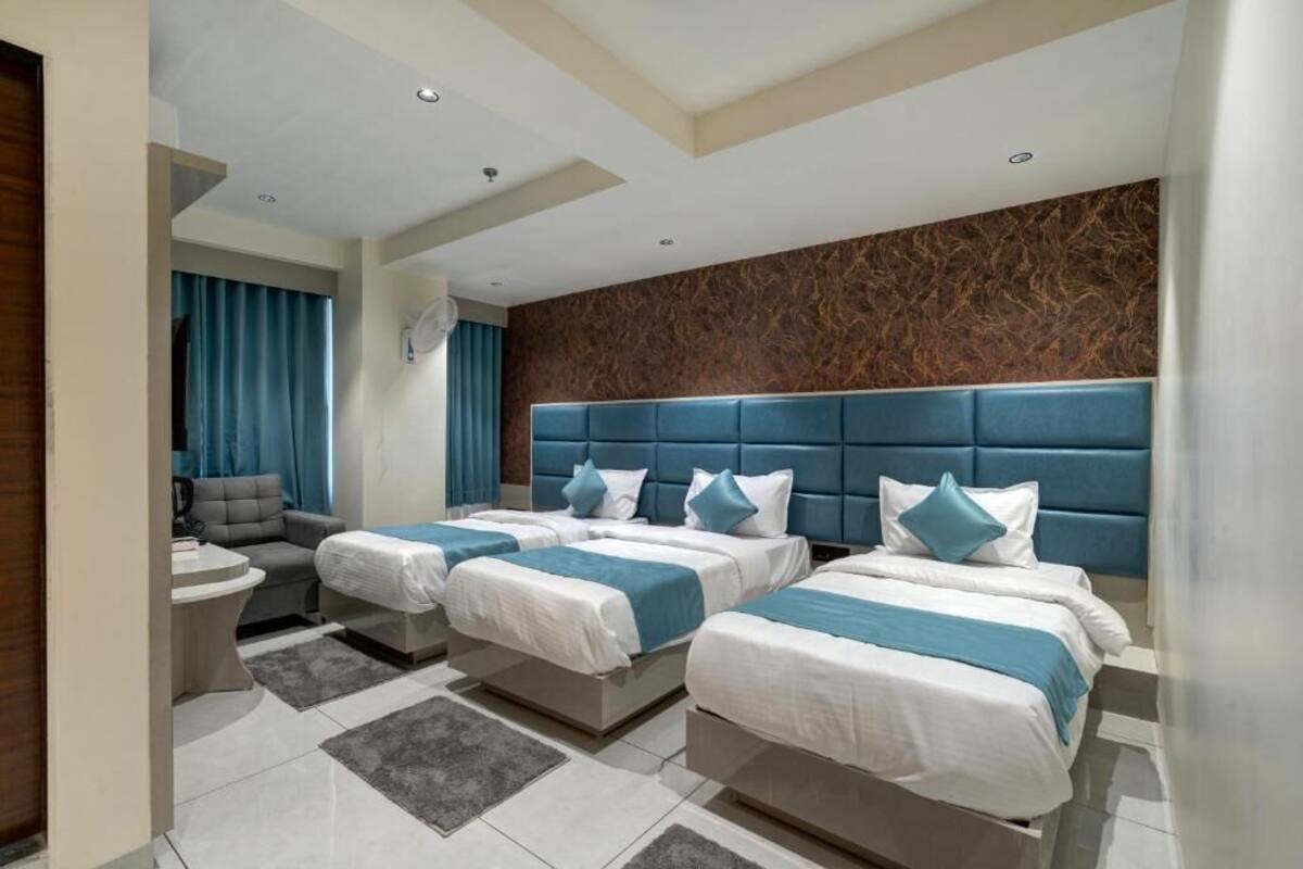 Une chambre d’hôtel avec trois lits, un canapé, une petite table et une salle de bain.