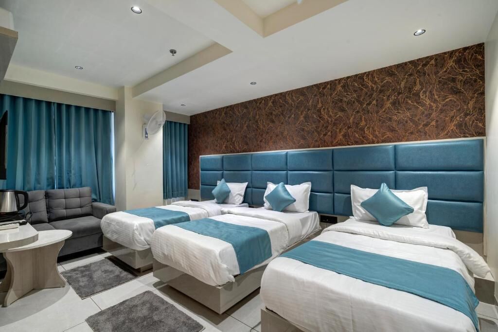 Ein Hotelzimmer mit drei Betten, einer Couch, einem kleinen Tisch und einer Wandverzierung.