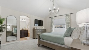 A bedroom with a bed, a dresser, a vanity, a television, and a chandelier. - Group Getaway with Games & Hot Tub! (Loveland)