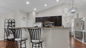 A spacious kitchen with dark cabinets, a central island with bar stools, and a hanging light fixture. - Group Getaway with Games & Hot Tub! (Loveland)