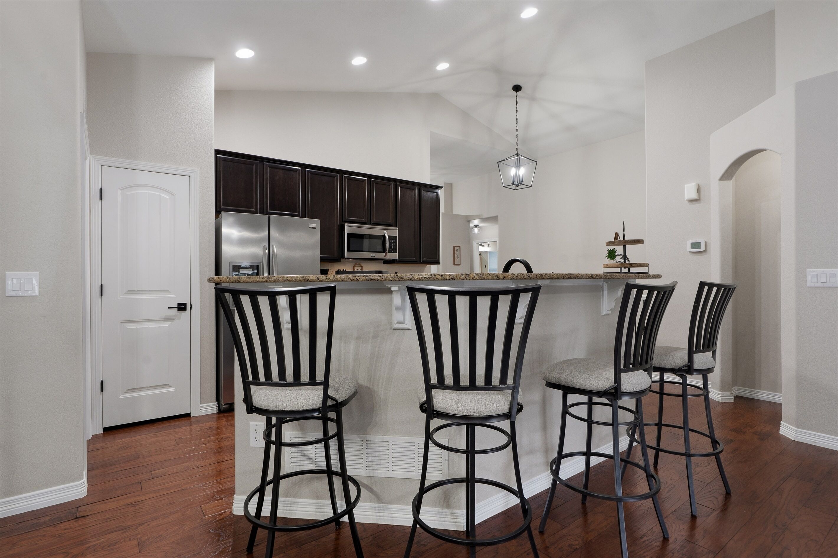 A modern kitchen with dark cabinets, stainless steel appliances, and a bar area with stools.