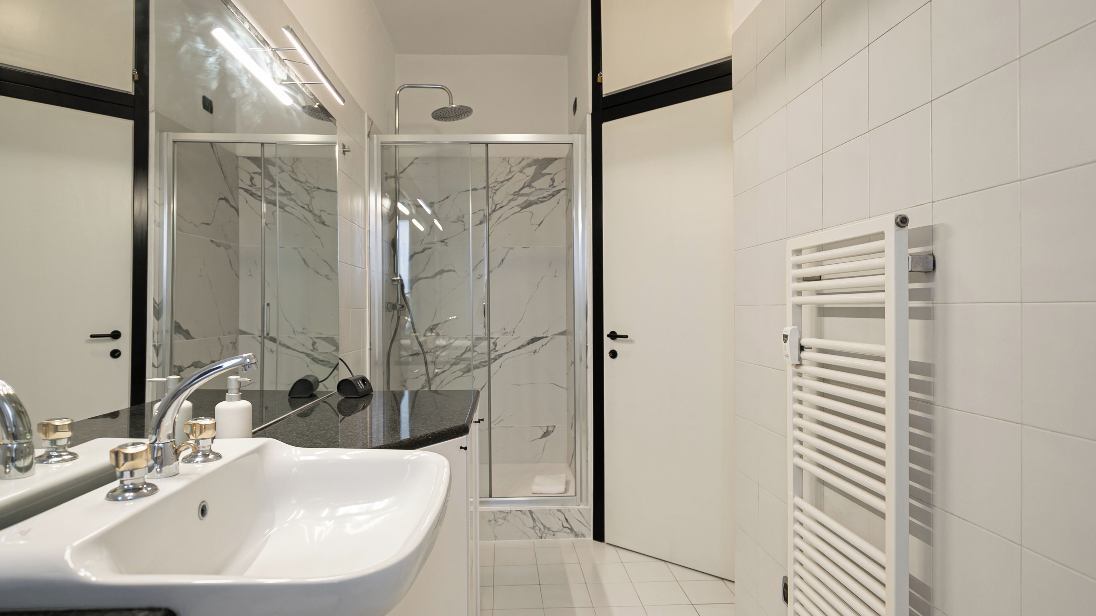 Ein modernes Badezimmer mit einem weißen Waschbecken, einer Duschkabine aus Glas und einem weißen Handtuchhalter.