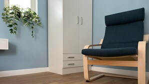 A room with a wooden floor, a blue chair, a white wardrobe, and a hanging plant. - The Attico (Bari)