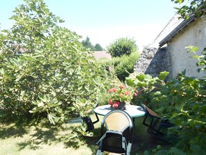 A garden with a table and chairs, surrounded by greenery and a stone wall.