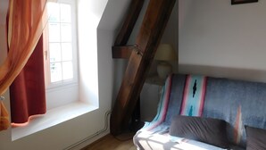 A room with a sloped ceiling, a window with a sheer curtain, a bed with a colorful blanket, and a lamp on a bedside table. - Loré Cottage Near Amboise and Chenonceaux (Montlouis-sur-Loire)