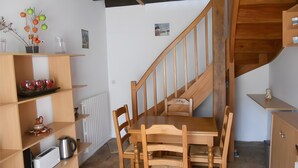 A wooden dining table with chairs, a wooden staircase, and a shelf with kitchen items. - Loré Cottage Near Amboise and Chenonceaux (Montlouis-sur-Loire)