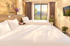 Une chambre d’hôtel avec un grand lit, une petite table avec une bouilloire, un vase de fleurs et une vue sur la verdure par la fenêtre.