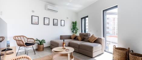 Een moderne woonkamer met een bank, stoelen, een salontafel en een groot raam.