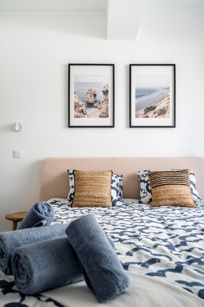 Un lit bien fait, avec des serviettes pliées en rouleaux, une tête de lit et deux tableaux encadrés accrochés au mur.