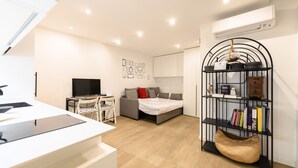 Une pièce moderne et bien éclairée, dotée d’un téléviseur à écran plat, d’un canapé avec des coussins, d’une bibliothèque et d’un bureau avec une chaise.