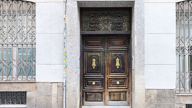 Une porte en bois à deux battants, ornée de motifs métalliques complexes, et une entrée encadrée de pierres.