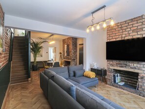 A modern living room with a brick fireplace, a large sectional sofa, and a flat-screen TV mounted on the wall. - Ty Gelert (Conwy)