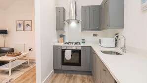 Een kleine keuken met grijze kastjes, een gasfornuis, een magnetron en een spoelbak.
