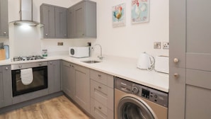 Een moderne keuken met grijze kastjes, een inbouwoven, een wasmachine en een spoelbak.