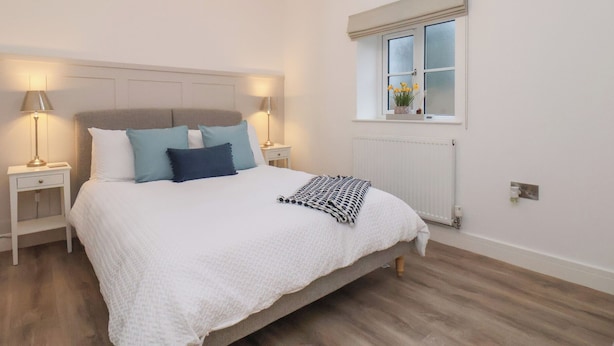 Een slaapkamer met dakraam, een raam met bloemen, een bed met witte beddengoed en blauwe kussens, en bedlampen.