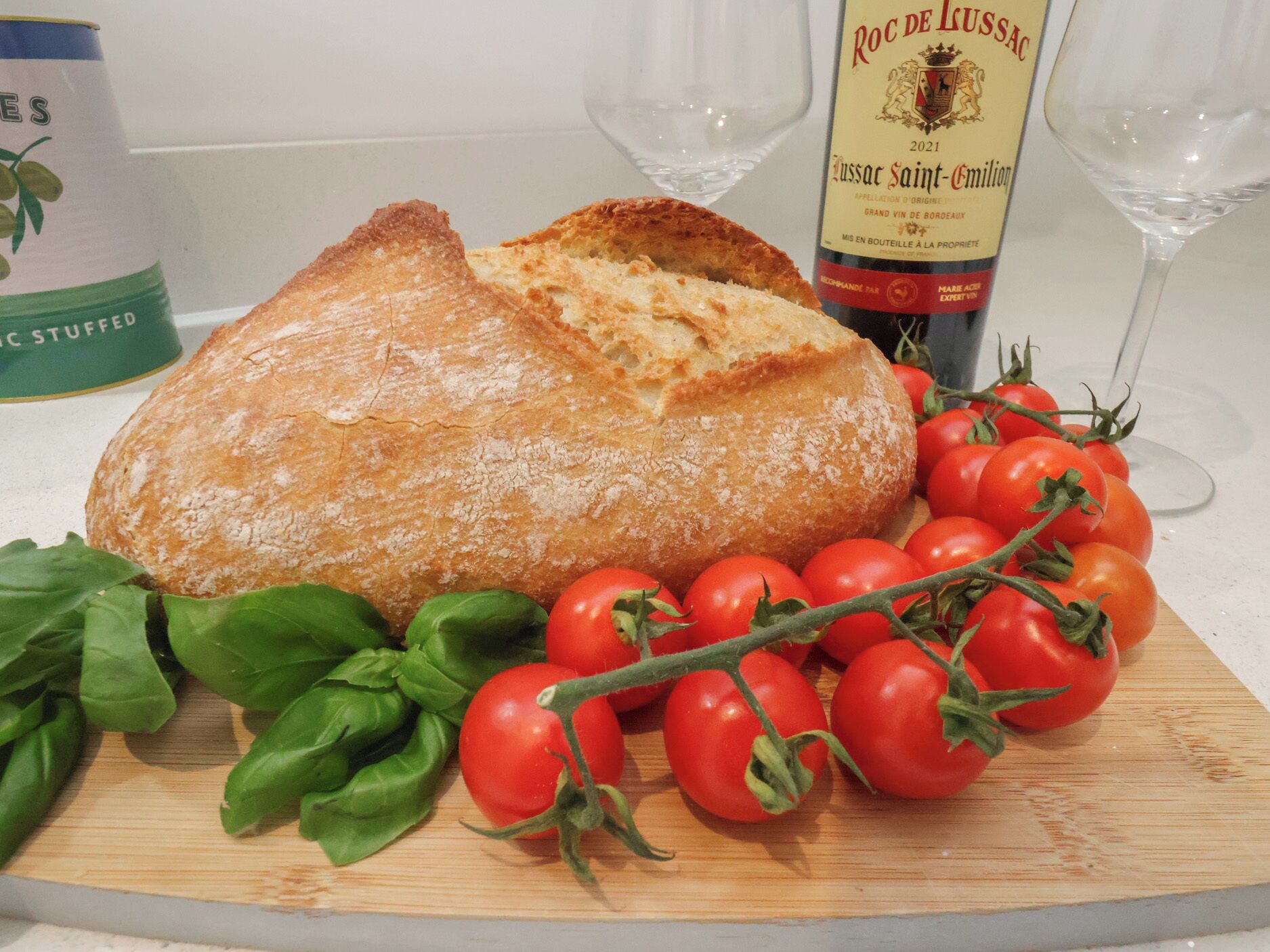 A loaf of bread, fresh tomatoes, and basil leaves on a wooden board.
