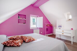 A bedroom with a sloped ceiling, a bed with patterned pillows, a white dresser, and a pink wall. - Apartment 'La Casetta Rosa' (Martina Franca)