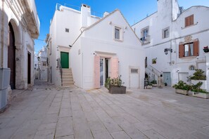 Une rue étroite bordée de bâtiments blancs, avec une porte verte et des plantes en pot.