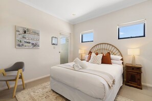 A bedroom with a large bed, two bedside tables, a chair, and a wall-mounted artwork.