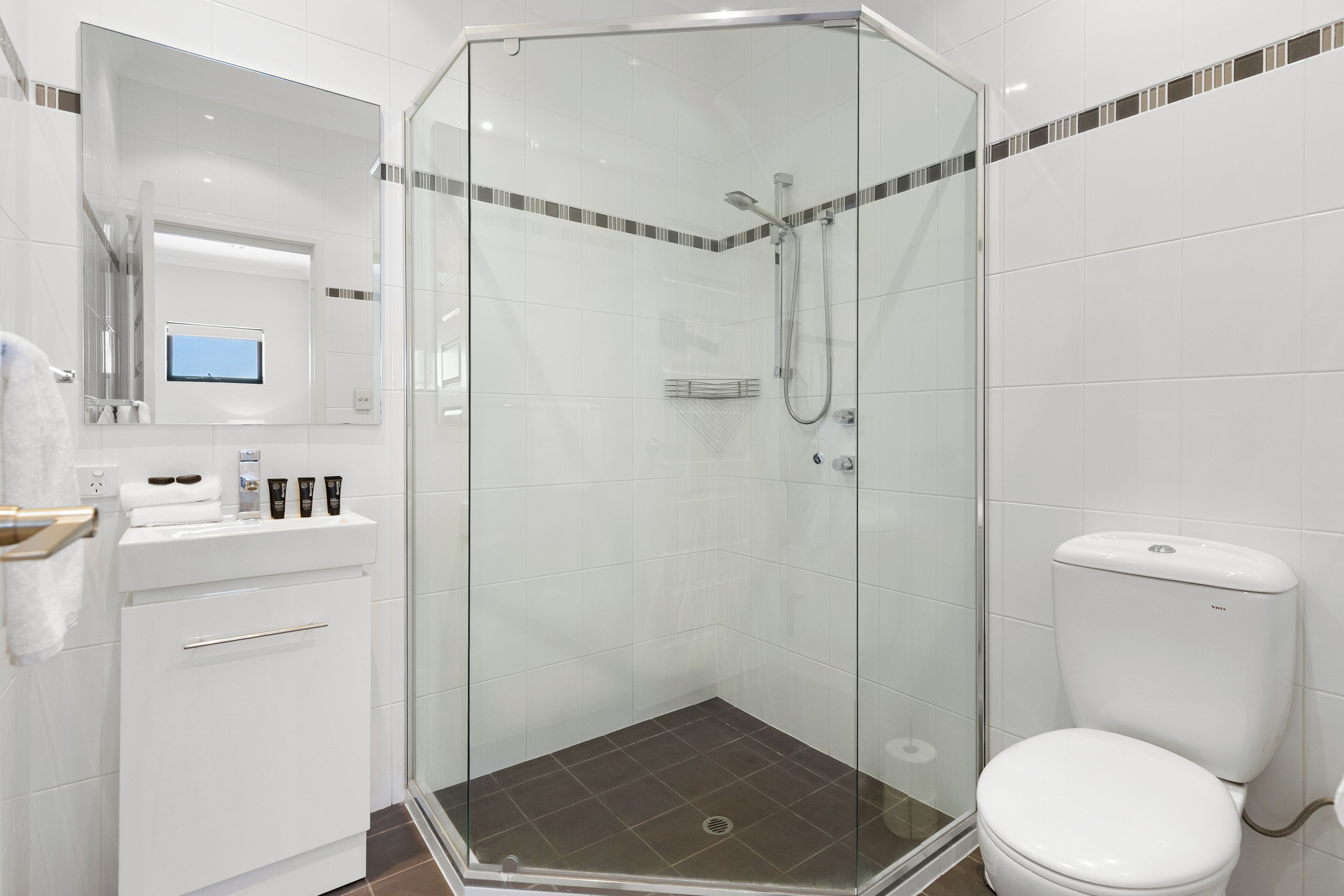 Une salle de bain moderne avec une douche à parois de verre, des toilettes et un meuble-lavabo doté d’un miroir et d’une petite fenêtre.