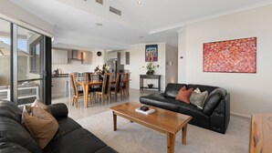 Una sala de estar moderna con un sofá de cuero negro, una mesa de centro de madera y un comedor con sillas y una mesa de madera.