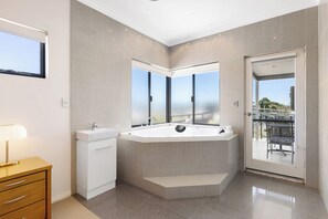 A modern bathroom with a large bathtub, a vanity with a sink, and a mirror. There is a window providing a view of the outdoors.