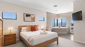 Un dormitorio moderno con una cama grande, mesitas de noche, un televisor de pantalla plana y un baño con bañera y ducha.