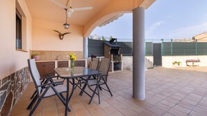 Une terrasse couverte avec une table et des chaises, un ventilateur de plafond et un mur en pierre.