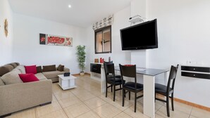 Un salon moderne comprenant un canapé, une table à manger, des chaises, un téléviseur à écran plat et une plante en pot.