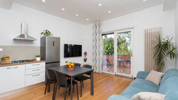 A modern kitchen with white cabinets, a stainless steel refrigerator, and a dining area with a table and chairs. - YourHome - Lady Lucy Holiday Home (Meta)