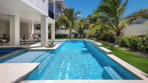 Une piscine rectangulaire à l’eau d’un bleu limpide, entourée d’un bâtiment blanc doté de balcons, de palmiers et d’une pelouse bien entretenue.