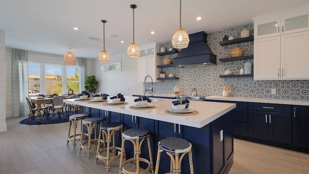 Une cuisine moderne dotée d’un grand îlot central, de tabourets de bar, de luminaires suspendus et d’étagères décoratives.