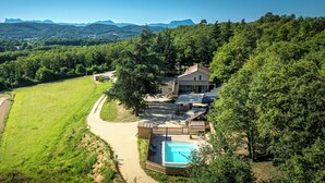 Une grande maison avec une piscine, entourée d’une végétation luxuriante et de champs.