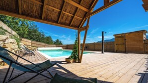 Une terrasse en bois avec des chaises longues, une piscine et un abri de jardin en bois.