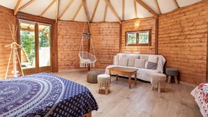 L’intérieur d’un chalet confortable, avec un canapé, un fauteuil suspendu et un grand lit.