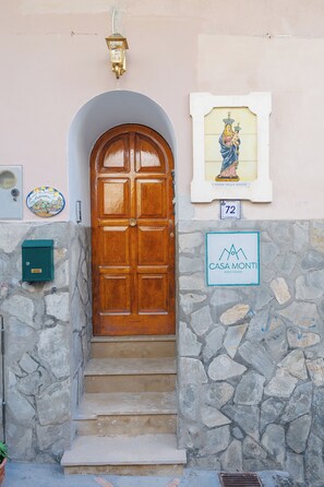 A wooden door with a stone wall, a sign reading "Casa Monti Positano," and a framed picture above the door. - Casa Monti Positano (Montepertuso)