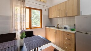 A compact kitchen with wooden cabinets, a stainless steel refrigerator, and a window with a view of greenery. - Tirana Central Apartment - Free Parking - Fit Five (Tiranë)