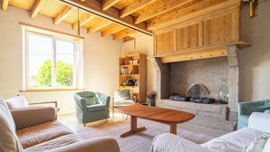 Uma sala de estar acolhedora, com lareira, vigas de madeira no teto e uma janela grande.
