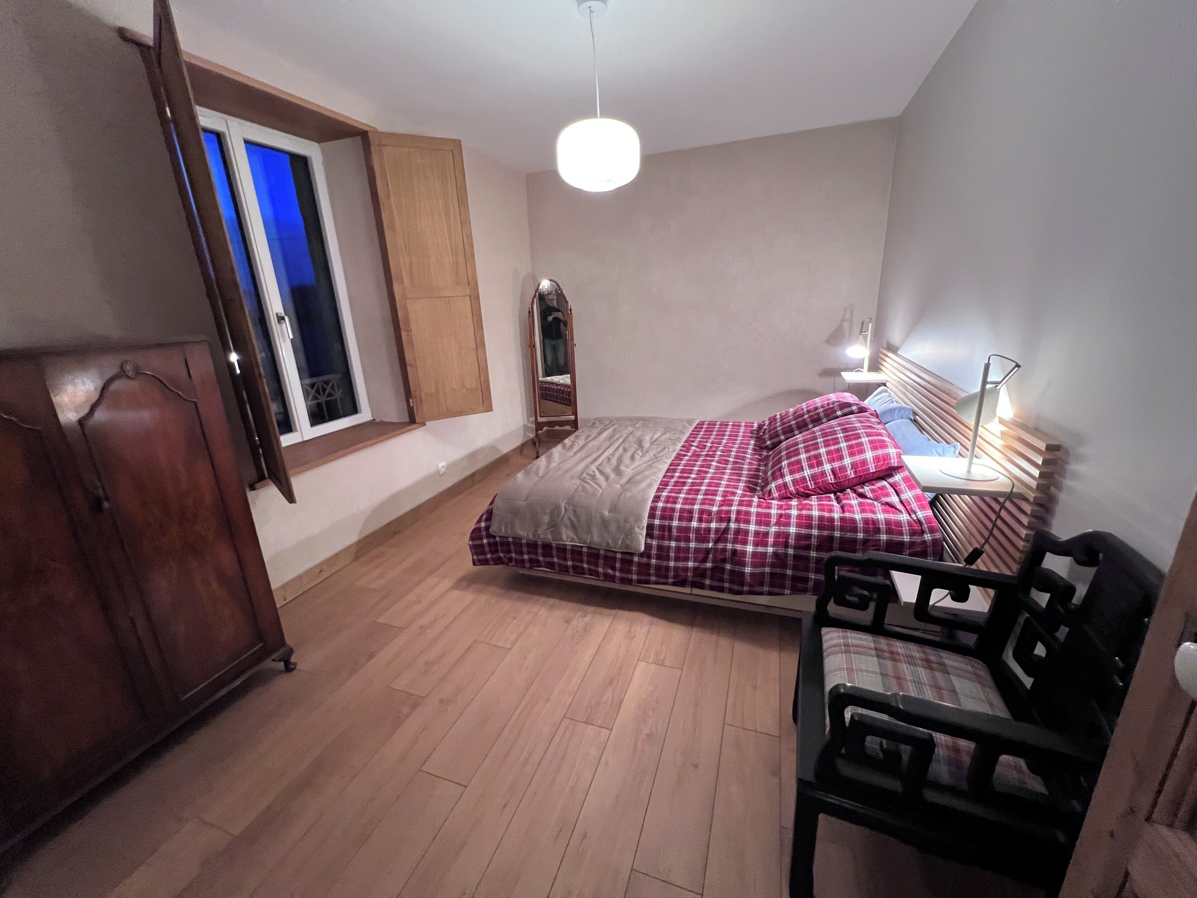 Une chambre à coucher comprenant un lit, une armoire en bois, un bureau avec une chaise, une table de chevet avec une lampe et une fenêtre donnant sur l’extérieur.