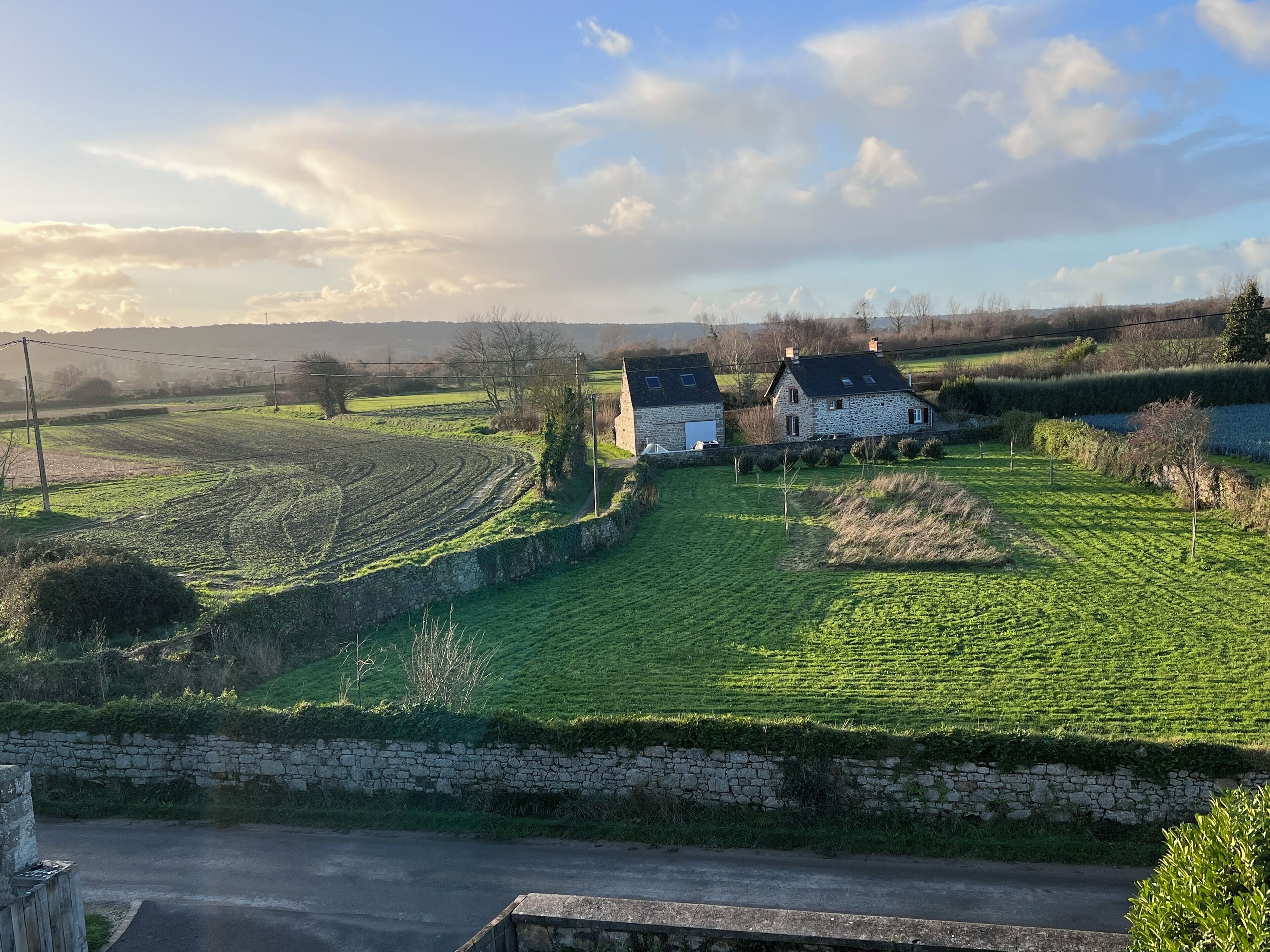 A rural landscape with stone houses, green fields, and a stone wall.