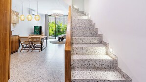 A modern interior with a dining area, a staircase, and a view of greenery. - Ocean Breeze Berawa Villa (Canggu)