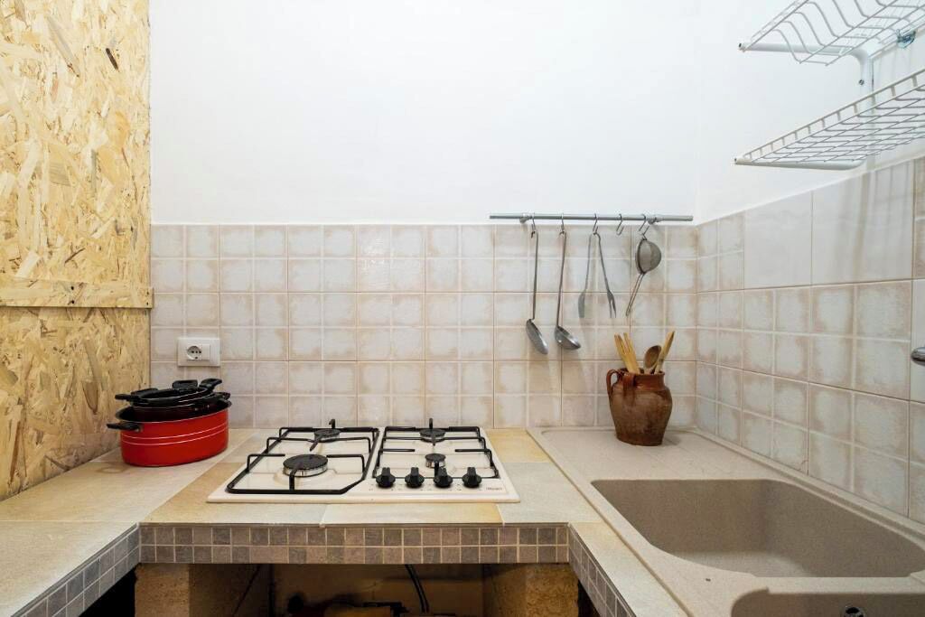 A kitchen with a gas stove, a red pot, a sink, and a hanging rack with utensils.