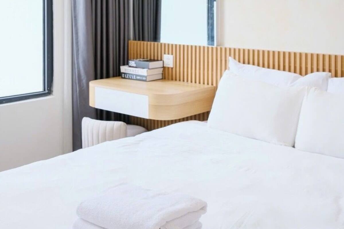 Ein Hotelzimmer mit einem Bett, einem Nachttisch mit Büchern, einem Spiegel und einem Fenster mit Vorhängen.